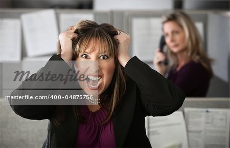 Frustrated female office worker in a cubicle pulls her hair