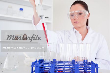 Pretty female biologist holding a manual pipette with sample from test tubes in a lab