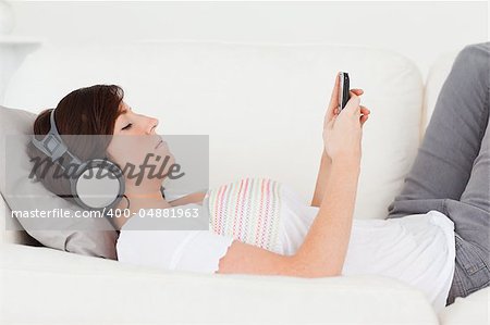 Good looking brunette woman writing a text on her mobile while lying on a sofa in the living room