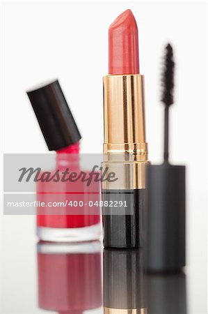 A mascara tube with a pale red lipstick and a nail polish flask against a white background