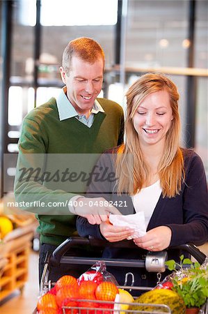 A happy couple looking at a grocery list in a supermarket