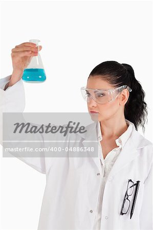 Dark-haired woman conducting an experiment while looking at a blue flask