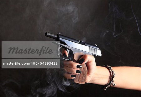 Black pistol in female hand on a background of a smoke
