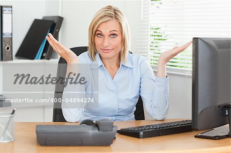 Young blonde woman sitting behind desk not having a clue what to do next in an office