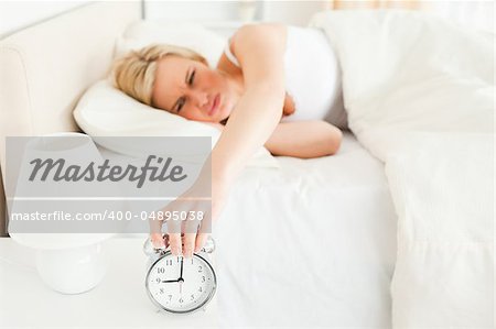 Tired woman switching off her alarm clockin her bedroom