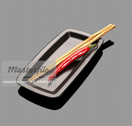 fresh red chili peppers on a plate with chopsticks over grey reflective surface