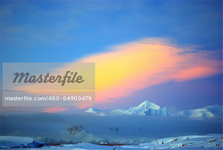 Covered with white snow mountain covered with clouds at sunset in Antarctica