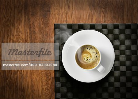 Steaming hot cup of espresso coffee with crema on wooden table and dark tablemat