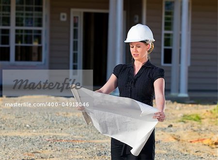 A female architect looking at blueprints at a residential construction site.