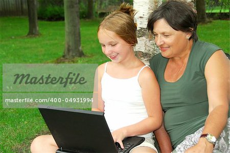 Grandmother and granddaughter sitting outside with laptop computer