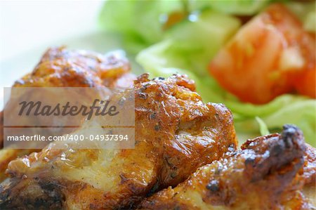 Grilled chicken on a white plate with vegetables on the background.