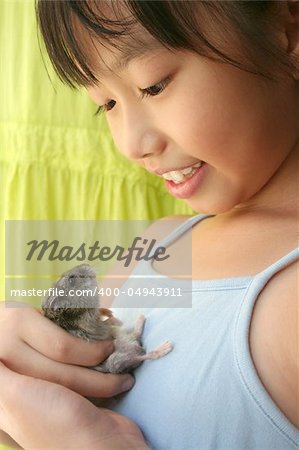 Girl smiling happily and playing with her grey pet hamster