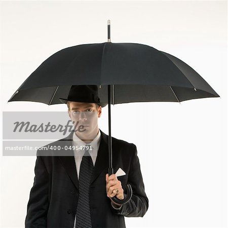 Caucasian mid-adult businessman wearing fedora holding umbrella  and looking at viewer.