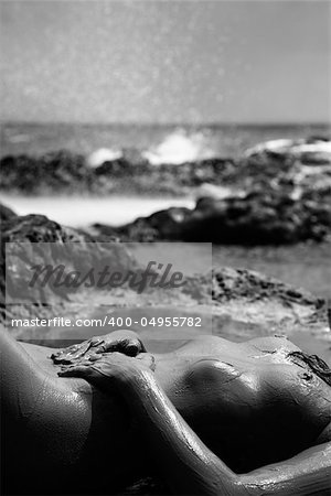 Young adult Caucasian female nude lying on rocky coast of Maui, Hawaii.