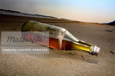 Half empty bottle of liqueur lies abandoned on a beach at sunset