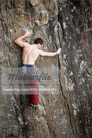 A male climber against a large rock face climbing lead.