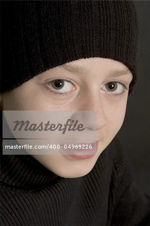 teeneage boy in black beenie hat agasint black backdrop