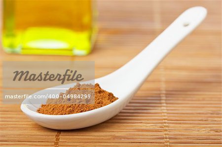 Cinnamon in the spoon and oil bottle for prepare tasty food with soft shadow in the bamboo mat background. Shallow depth of field