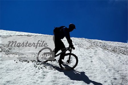 Sky, snow and mountain biker - downhill from mountain pass
