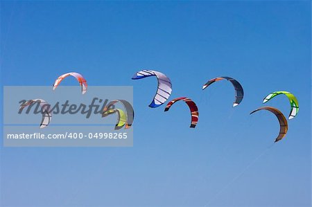 Nine surf kites in the air against a blue sky