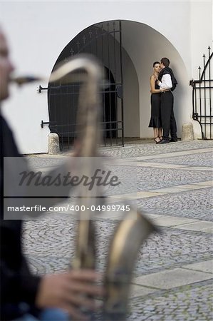 A street musician playing a saxophone serenades a romantic couple as the woman looks on thoughtfully