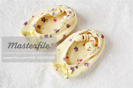 Small yellow children's bootees stand together on a white fabric