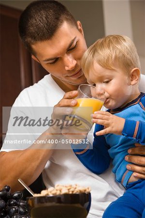 Caucasian man helping toddler son drink juice.