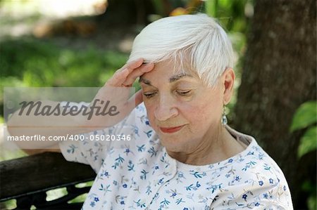 A senior woman massaging her temples.  She is sad and/or suffering from a headache.