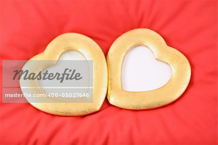 two gold hearts are situated on red pillow