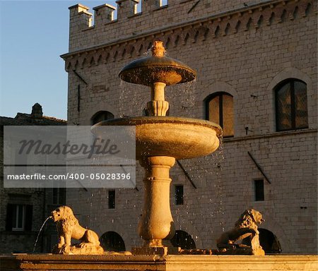 An old Italian fountain in the main town square of Assissi. Droplets of water from the fountain are highlighted in the warm golden glow of the evening just before sunset.