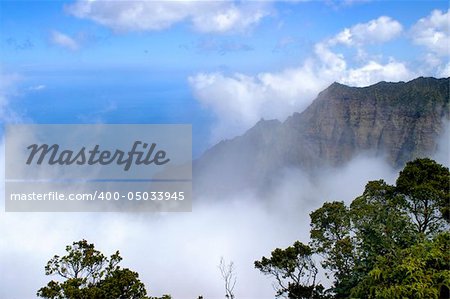 Beautiful Na Pali Coast is hugged by a large white cloud.  Vivid blue sky and water below.