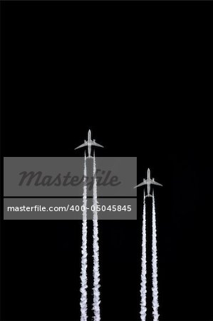 Two jet aircraft flying in a vertical parallel formation with smoke trails, set against a black sky background.