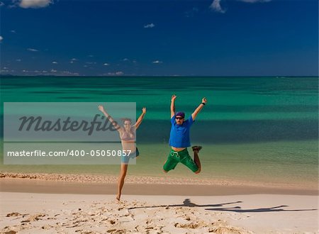 Young couple jumping on white sand beach by turquoise waters on tropical island