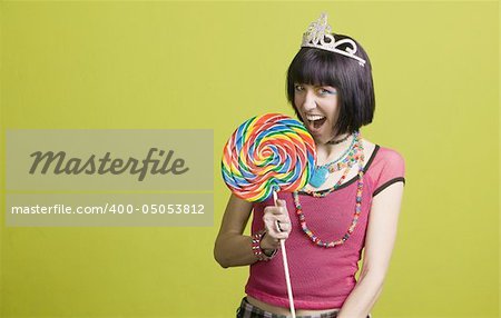 Pretty young woman takes a bite from a large lollipop