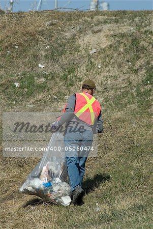 A man wearing a reflective vest, picking up spring garbage