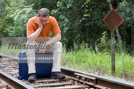 Tired man sitting on his suitcase on a railway
