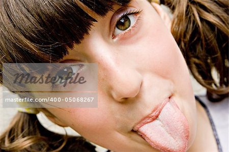 The brown-eyed dark-haired girl-teenager looks directly in a shot and puts out the tongue