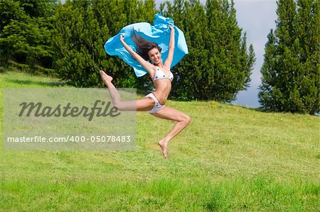 young woman jumping in a field with a blue scarf and white bikini