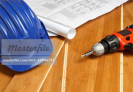 blue helmet, red drill and bluprint on wood floor