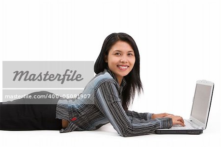 A beauty woman faing the camera while lie down on floor and typing on a laptop.