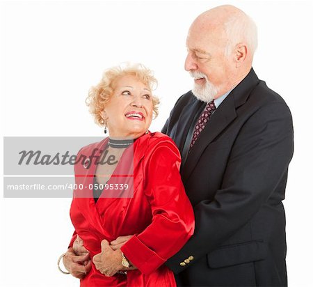 Senior couple look lovingly into each others eyes as they dance.  Isolated on white.