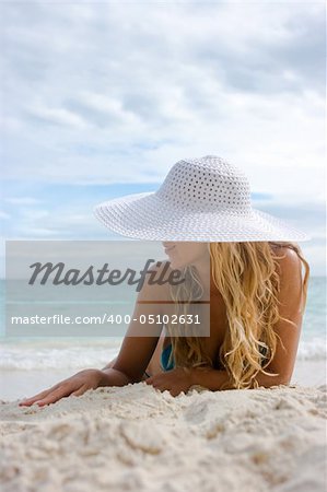 Beautiful blonde lying on white sand beach in hat
