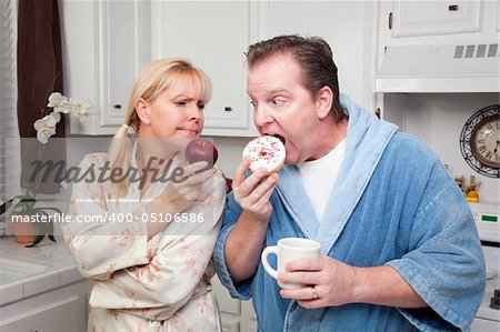 Couple in Kitchen Eating Donut and Coffee or Healthy Fruit.