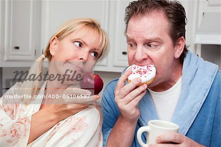 Couple in Kitchen Eating Donut and Coffee or Healthy Fruit.