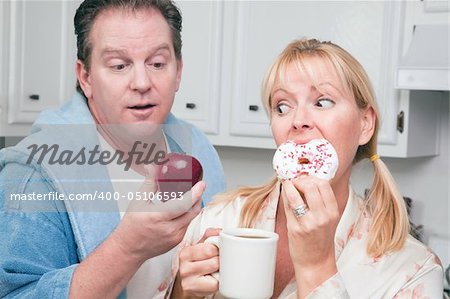 Couple in Kitchen Eating Donut and Coffee or Healthy Fruit.