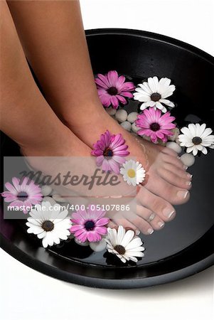 Beautiful pedicured feet and manicured hand with colorful spring daisies in a spa