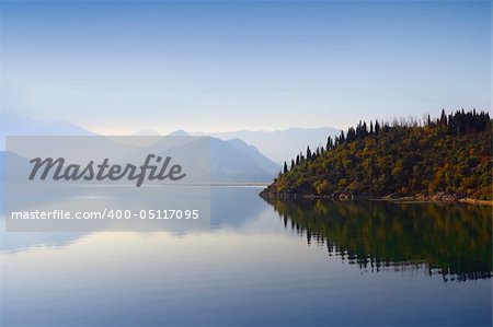 Mountain peaks covered with blue mist, still waterscape and autumn woods on the background in Montenegro.