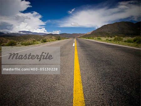 A desert road by the mountains surrounded by colorful nature.