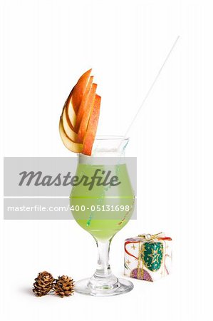 A view of a fancy cocktail glass filled with a delicious green drink and garnished with a sliced apple, a wrapped present and pine cones on a white background.