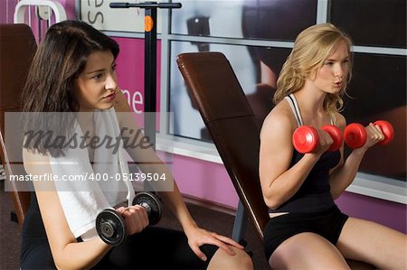 couple of girls doing free exercise with dumb-bells in front of mirror